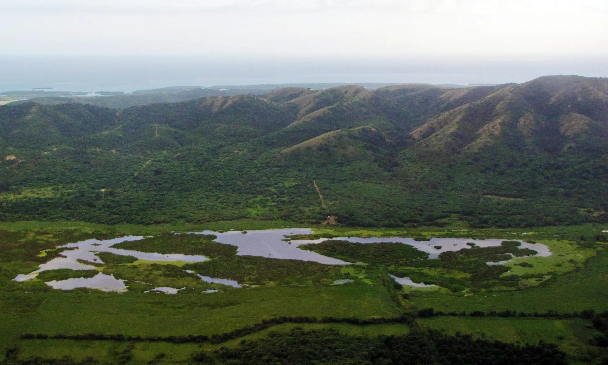 Aerial view of Laguna Cartagena: open water and green marsh at the foot of forested hills