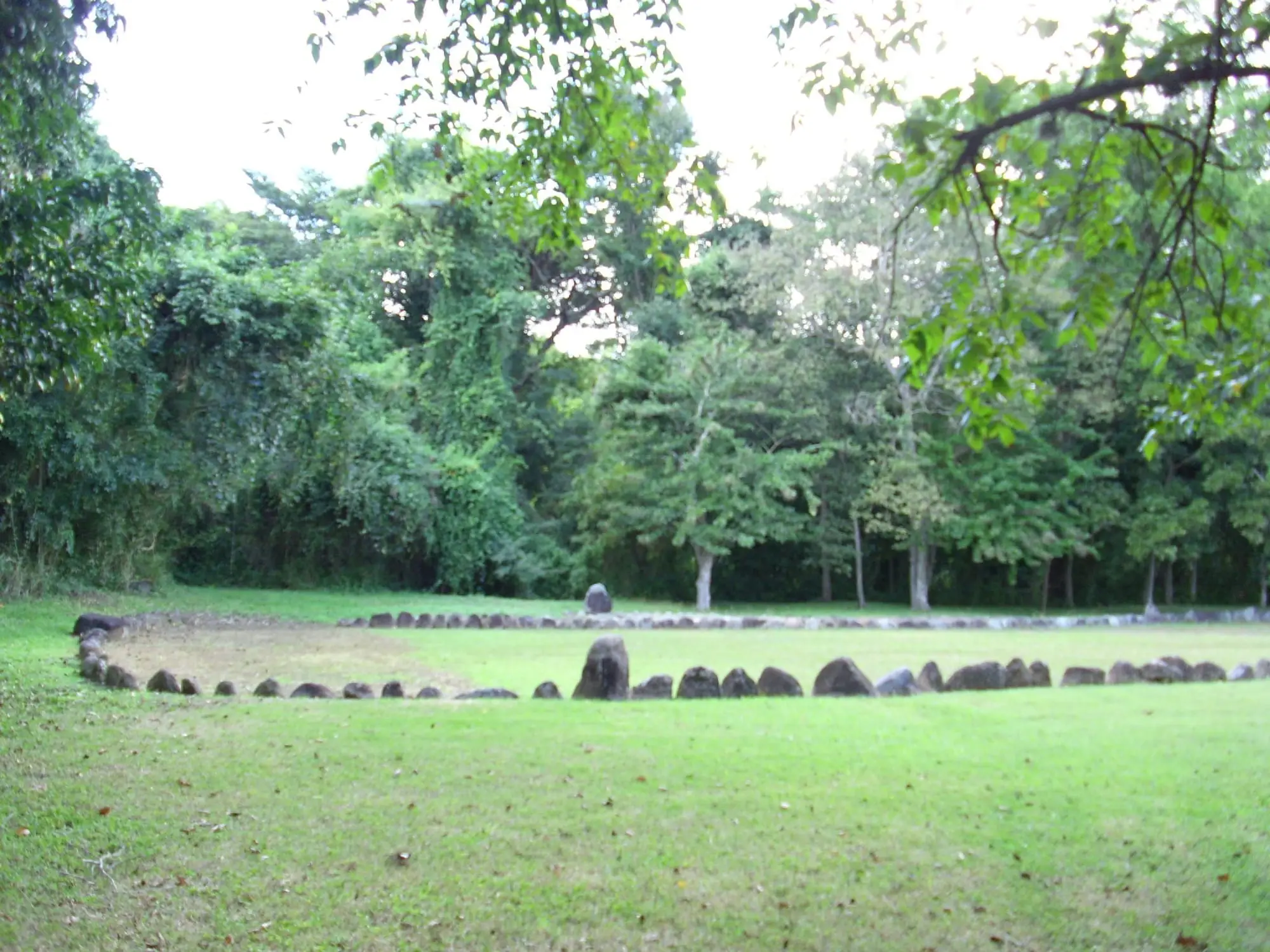 A Taíno ball court at Tibes, a grassy rectangle lined with upright stones under tall trees