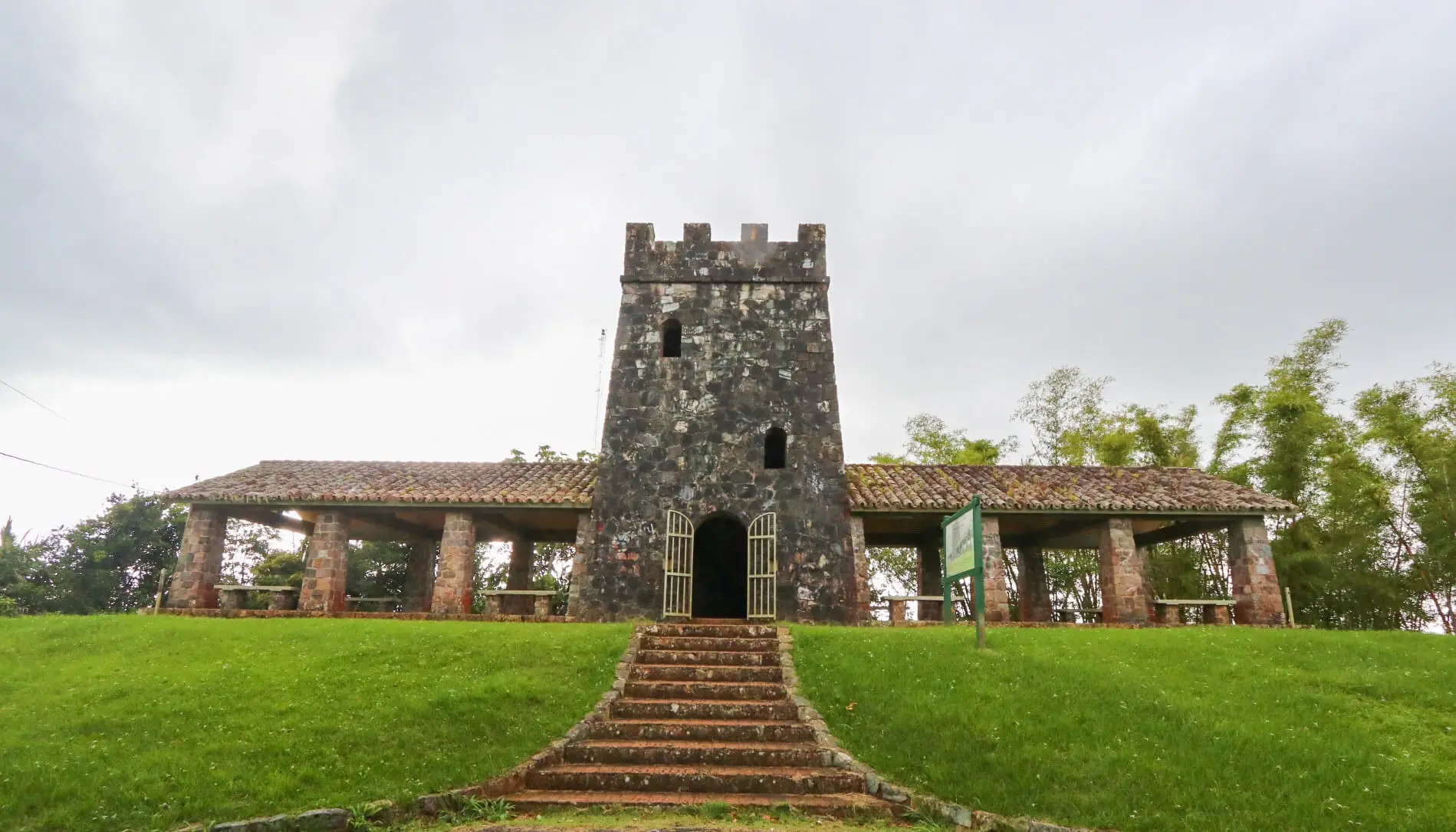 The stone lookout tower of Maricao with its battlements, steps and a covered shelter on a green lawn